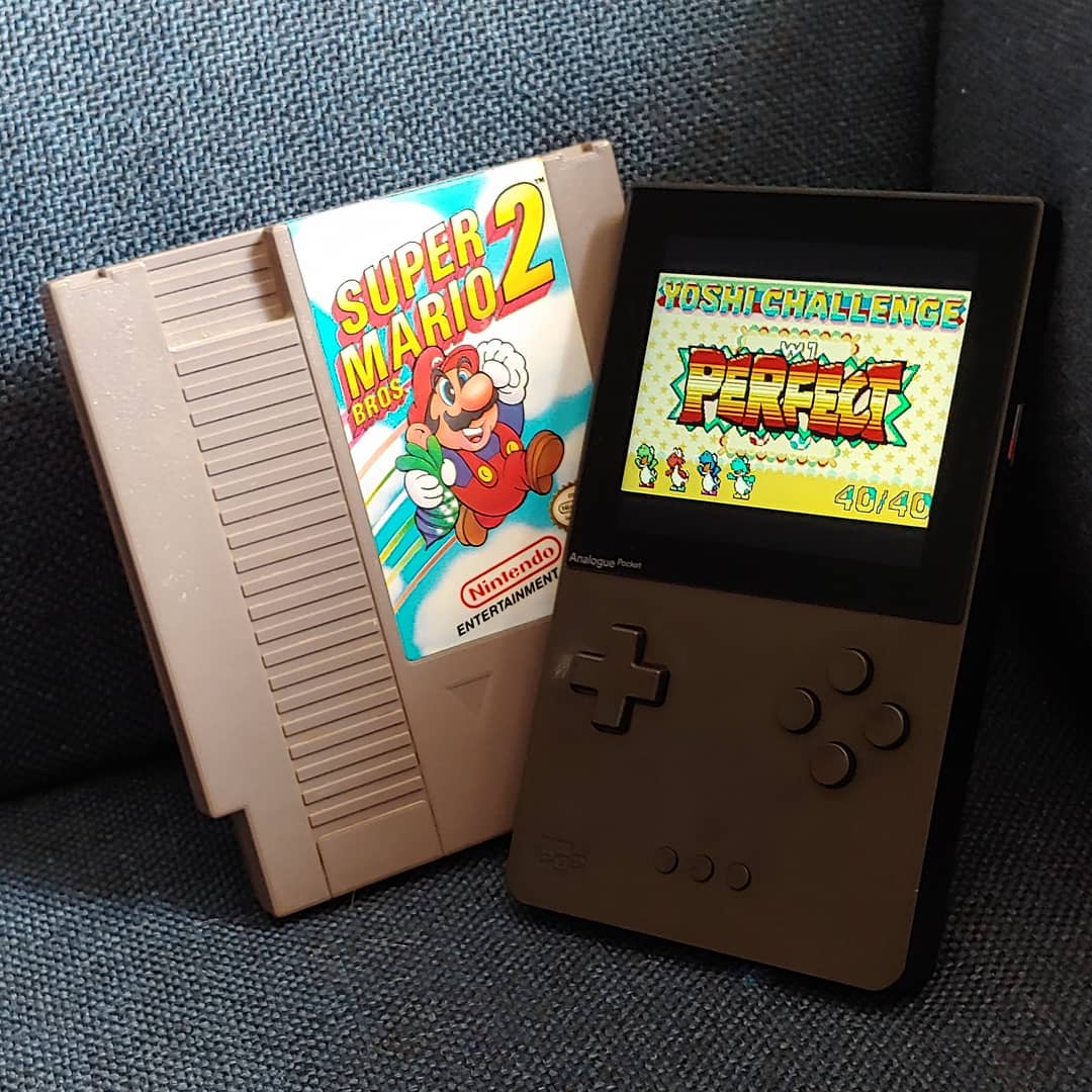 A photo of an NES cartridge of Super Mario Bros. 2 alongside an Analogue Pocket displaying the Perfect Yoshi Challenge screen of Super Mario Advance