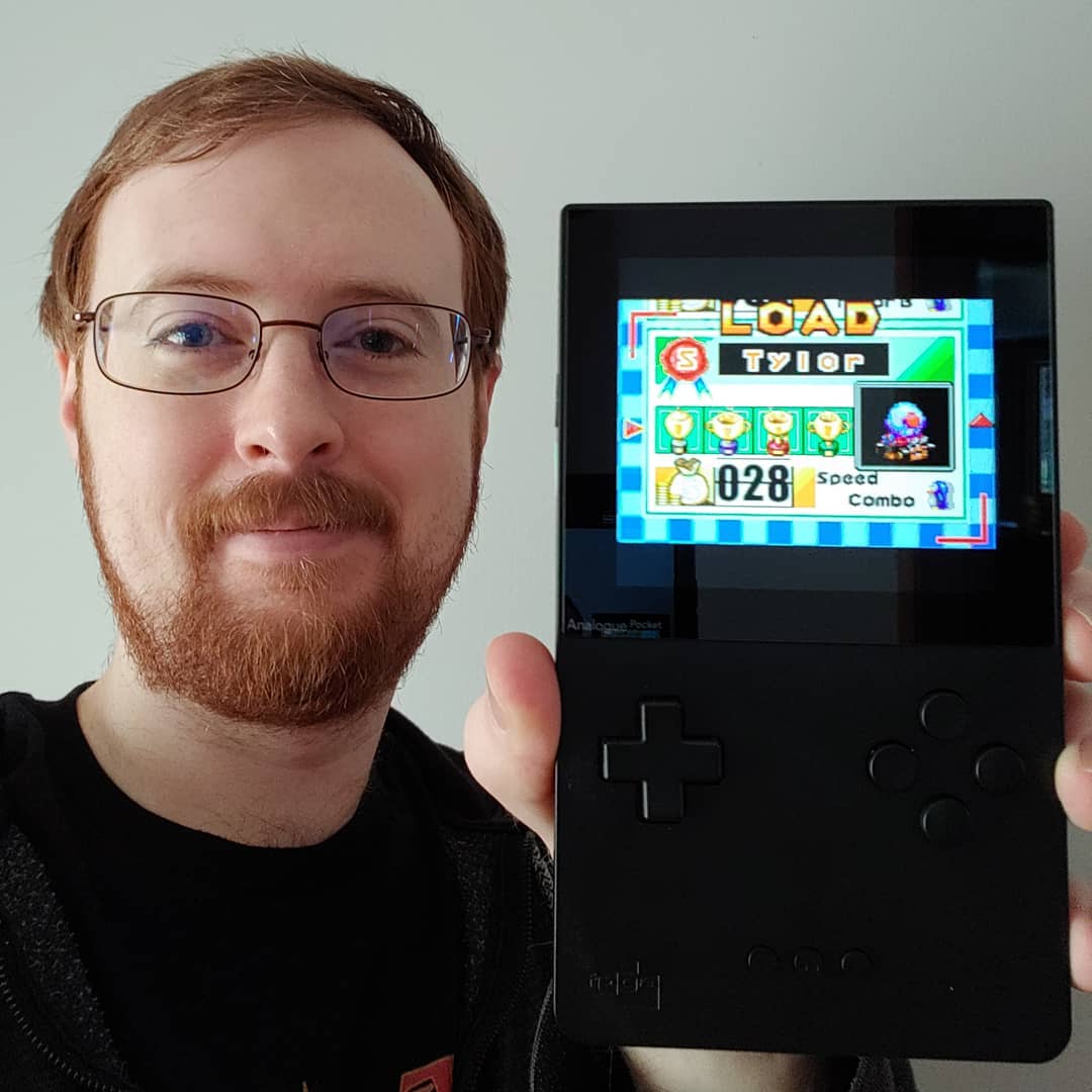 A photo of Tylor holding an Analogue Pocket displaying a completed save file for Krazy Racers